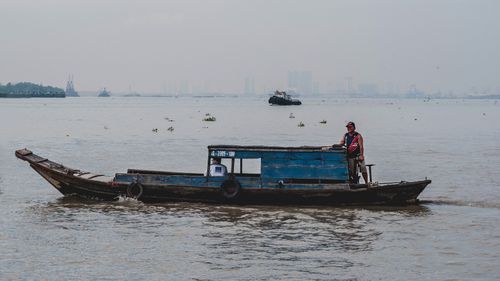 Free A fisherman navigates a rustic wooden fishing boat on a misty river, capturing a serene landscape. Stock Photo