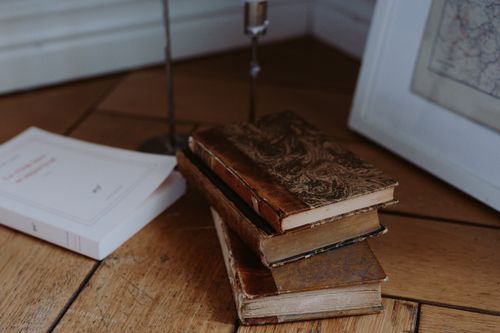 Free Stack of vintage books on a wooden floor in a cozy indoor setting with warm light. Stock Photo