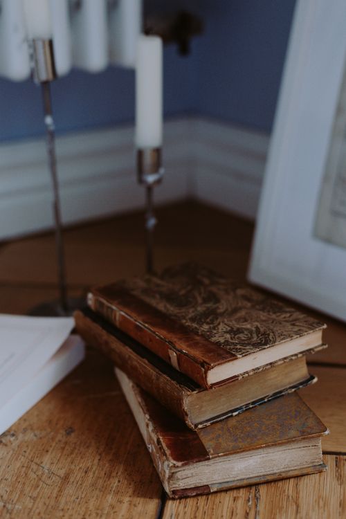 Free A stack of antique books with decorative covers on a wooden floor, enhanced by soft lighting. Stock Photo