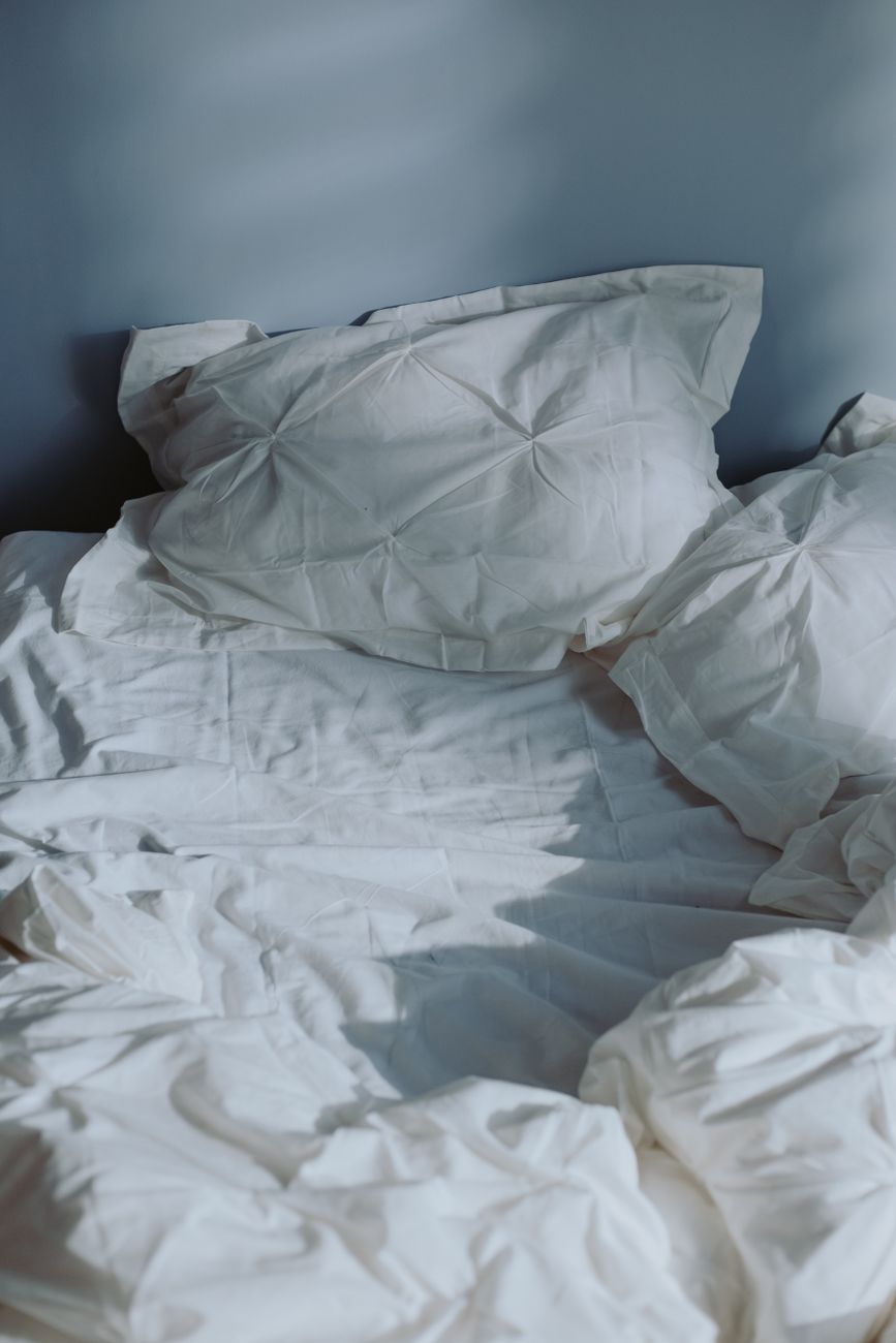 rumpled white bedding holding morning light across a half-made bed
