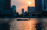 日落时分，船只航行在河上，与摩天大楼的天际线相映，展现了充满活力的城市生活