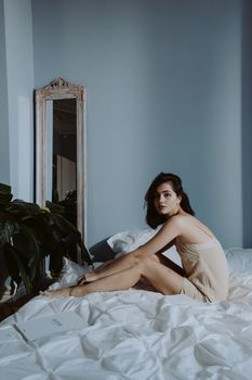 A stylish woman in lingerie sits on a bed in a chic indoor setting.