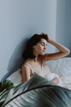 A tranquil woman seated on a bed, surrounded by soft linen, exudes calmness.