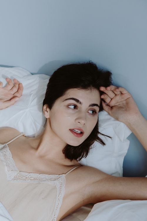 Free Portrait of a young woman lounging in elegant sleepwear on a bed, exuding calm and tranquility. Stock Photo