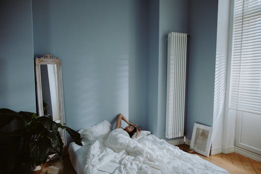 A woman relaxes on a white bed in a minimalist blue bedroom with natural light.