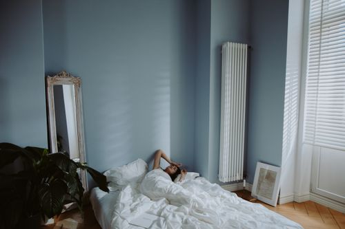 Free A woman relaxes on a white bed in a minimalist blue bedroom with natural light. Stock Photo