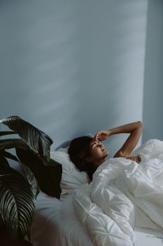 A woman relaxing in bed, surrounded by cozy bedding and soft morning light.