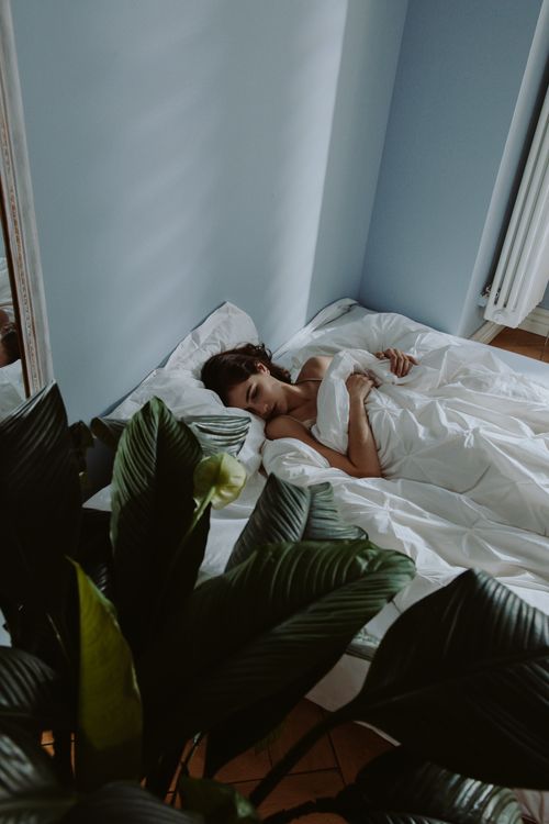 Free A woman peacefully sleeping on a bed surrounded by lush plants in a minimalist bedroom. Stock Photo