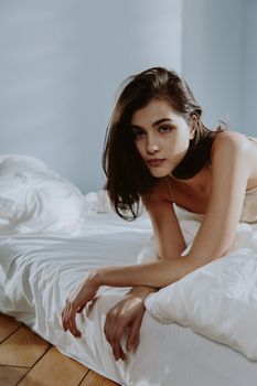Portrait of a woman lying on a bed, bathed in natural light, in a softly lit room.