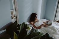 一名妇女在晨光下在床上看书，周围都是植物和倒影