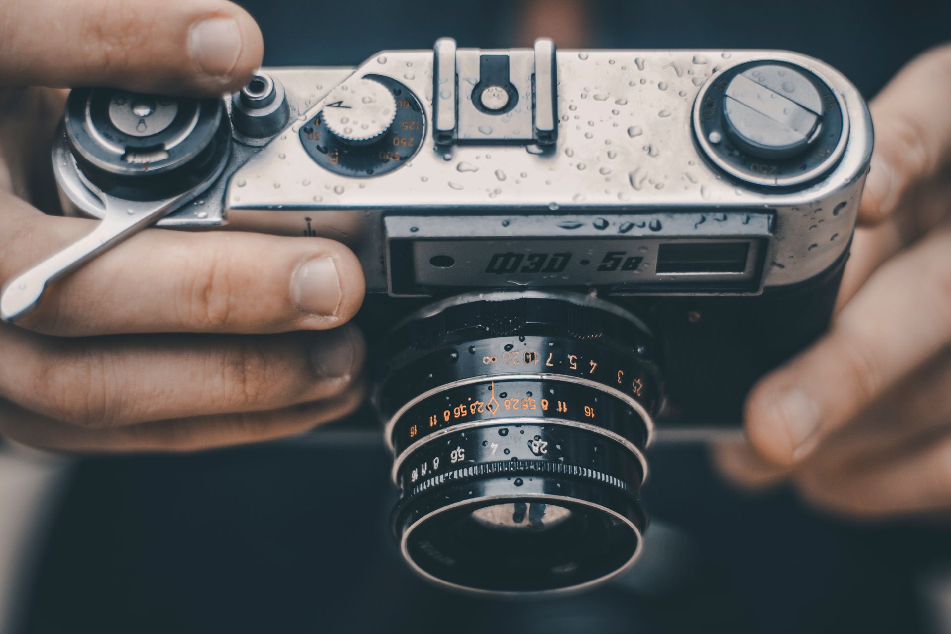 Close-up of hands holding a vintage analog camera covered in raindrops, showcasing a waterproof design.