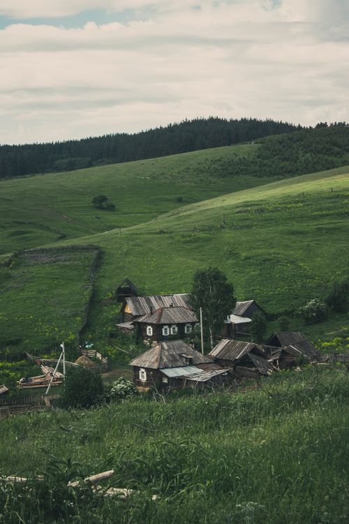 Free A picturesque rural scene featuring wooden houses nestled in a verdant valley surrounded by lush hills. Stock Photo