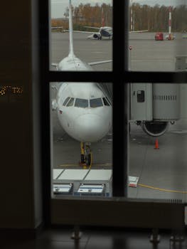 Aircraft parked at the gate of an airport, seen through a terminal window, ready for boarding.