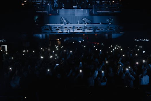 A lively concert scene with a crowd holding up smart phones and lights, creating an electrifying atmosphere.