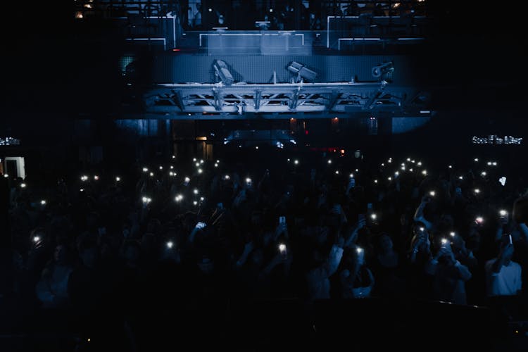 Crowd Of People Holding Glowing Smart Phones During A Concert