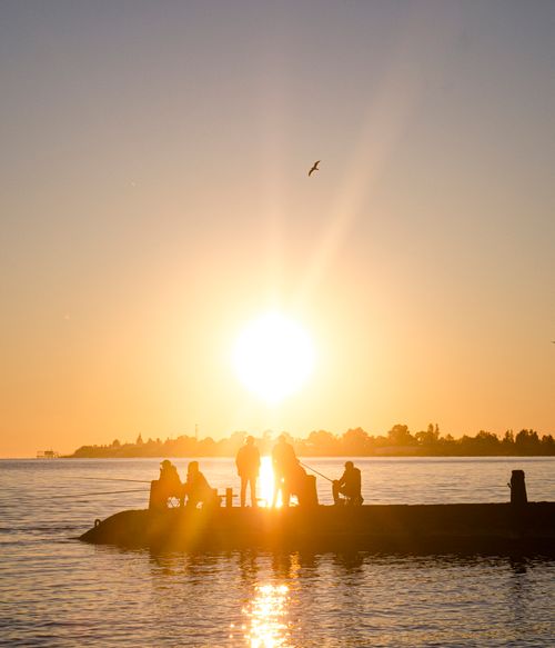 Free A serene scene of silhouetted fishermen on a pier with a vibrant sunset over calm waters. Stock Photo