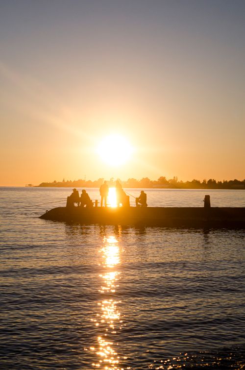 Free Silhouetted people on a dock with a stunning sunset reflecting over calm waters. Stock Photo