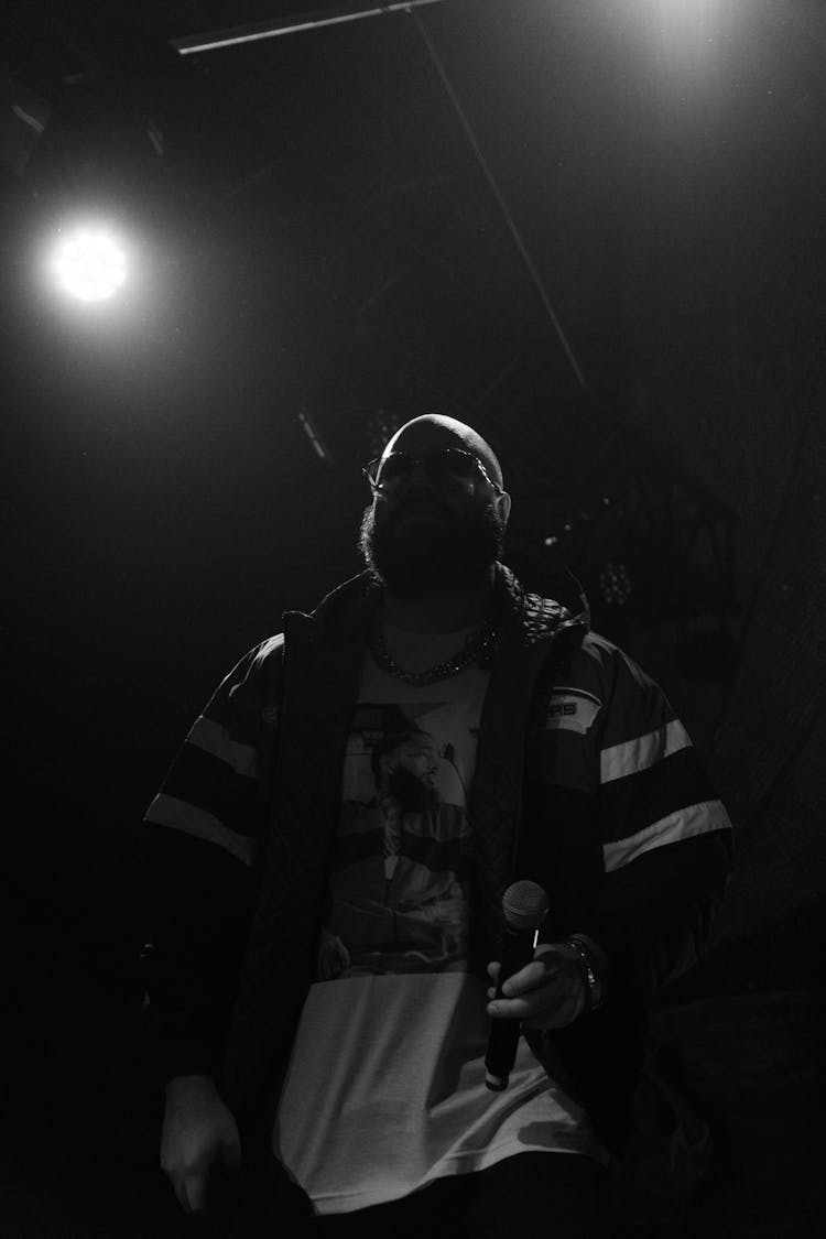 Black And White Shot Of A Man Holding A Mic On Stage