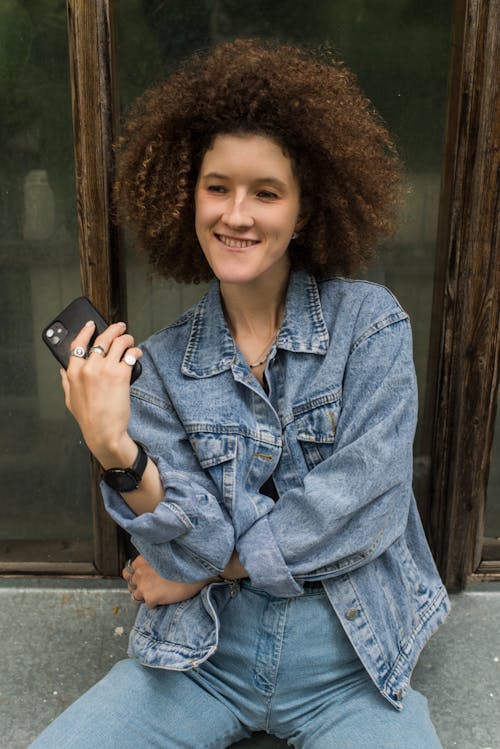 A Woman Wearing Denim Jacket and Jeans Holding a Smartphone