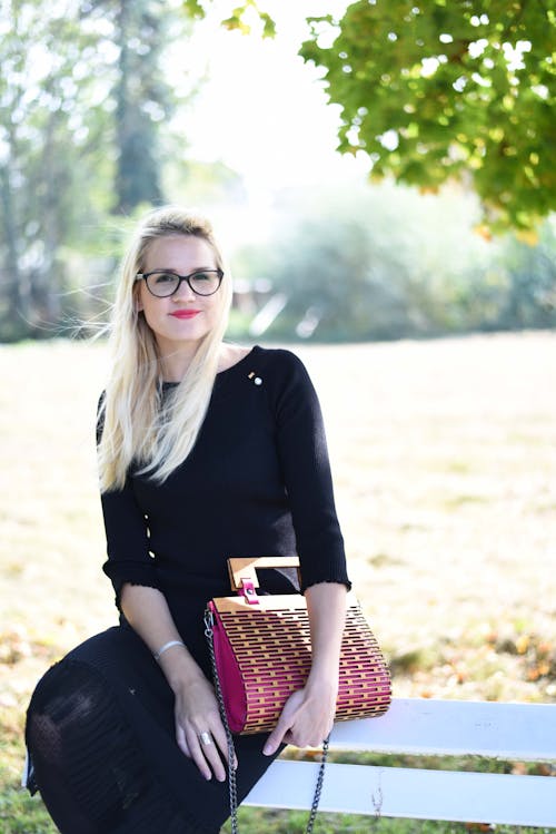 Free Woman in  Black Long Sleeves Sitting on a Wooden Bench while Holding a Pink Bag Stock Photo
