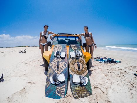 Women in swimsuits with surfboards by a yellow vehicle on a sunny beach.