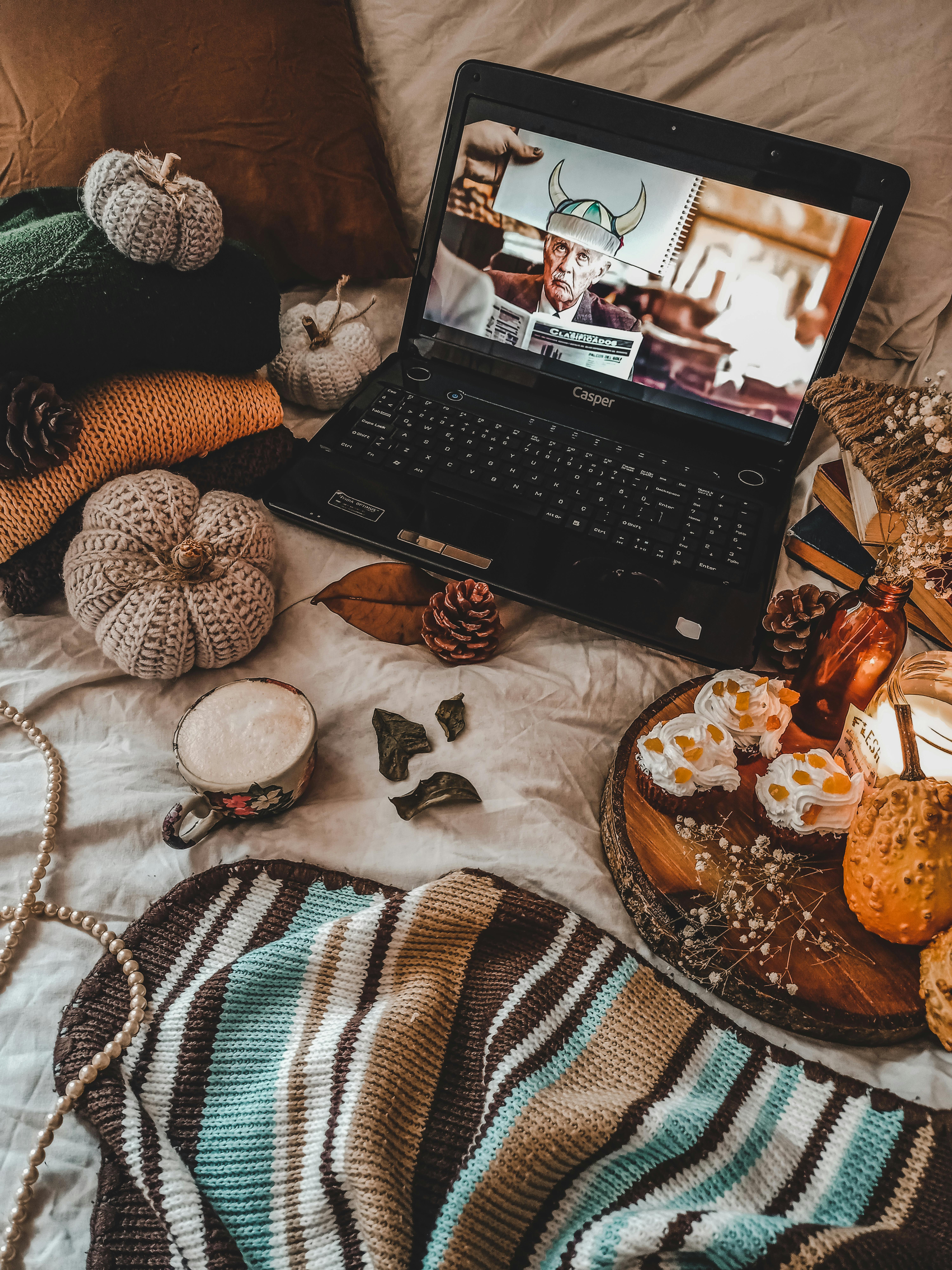 A cozy autumn setup featuring knitwear, pumpkins, a laptop, and pastries in a rustic home setting.