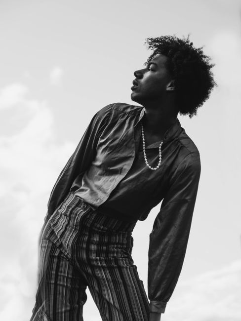 Black and white portrait of a fashionable man in a dynamic pose outdoors.