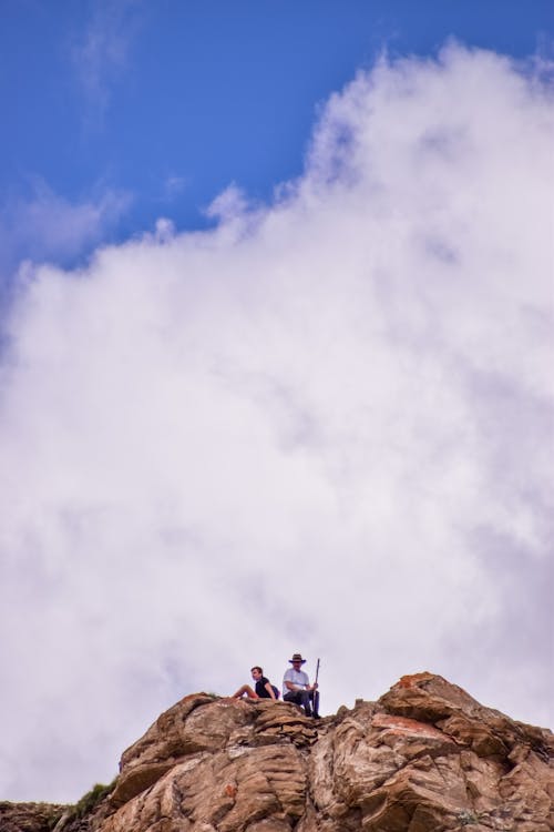 Free People Sitting on a Rock Formation Under the White Clouds and Blue Sky Stock Photo