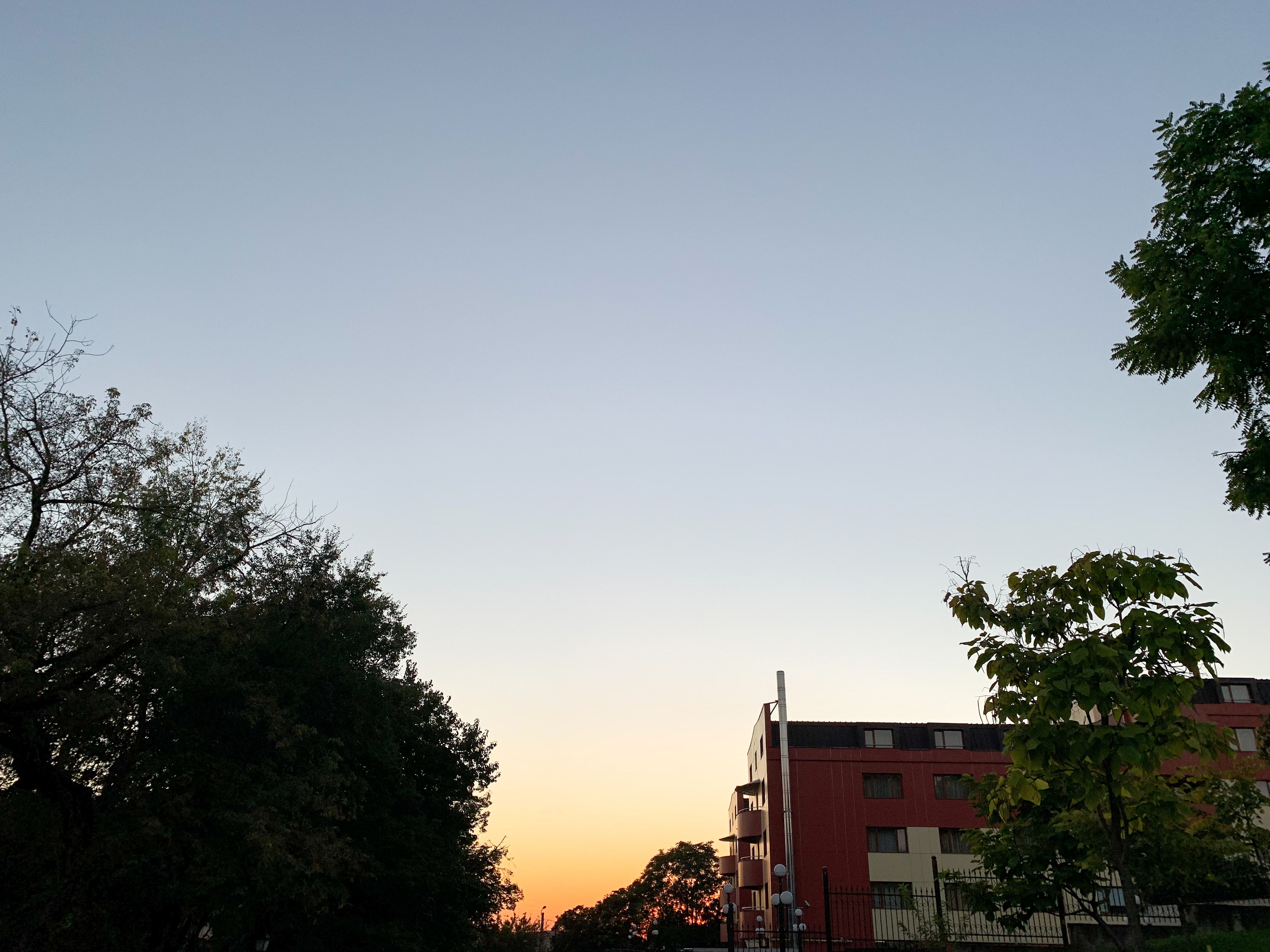 A serene sunset view with trees and a building silhouette against a colorful sky.