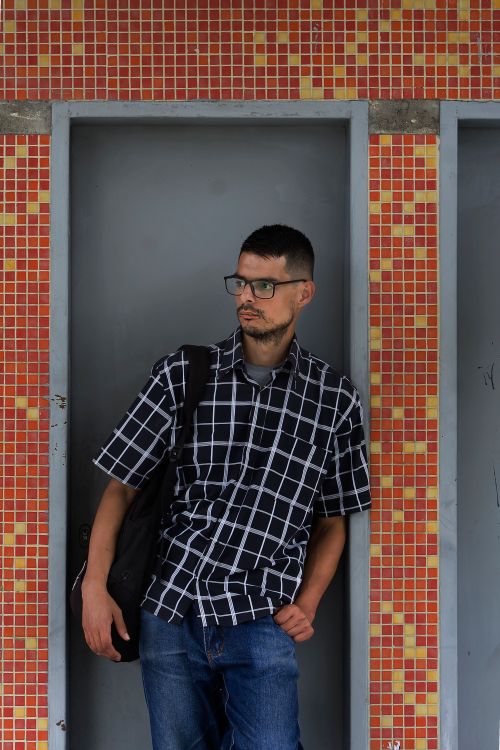 Free Stylish young man with glasses leans against an orange tiled wall, showcasing casual fashion. Stock Photo