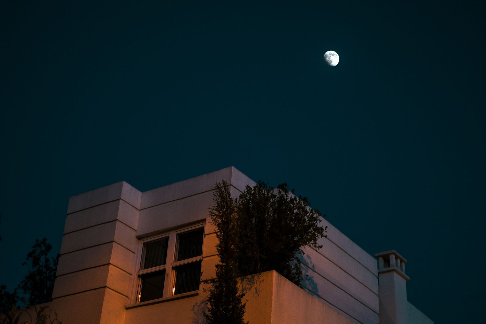 A modern house rooftop with a view of the moon in a clear night sky, showcasing architectural elegance.