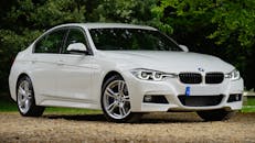 一辆白色宝马汽车停在绿树环绕的砾石路上，尽显豪华设计