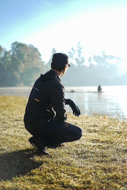 Man Crouching on Grass Near a Lake
