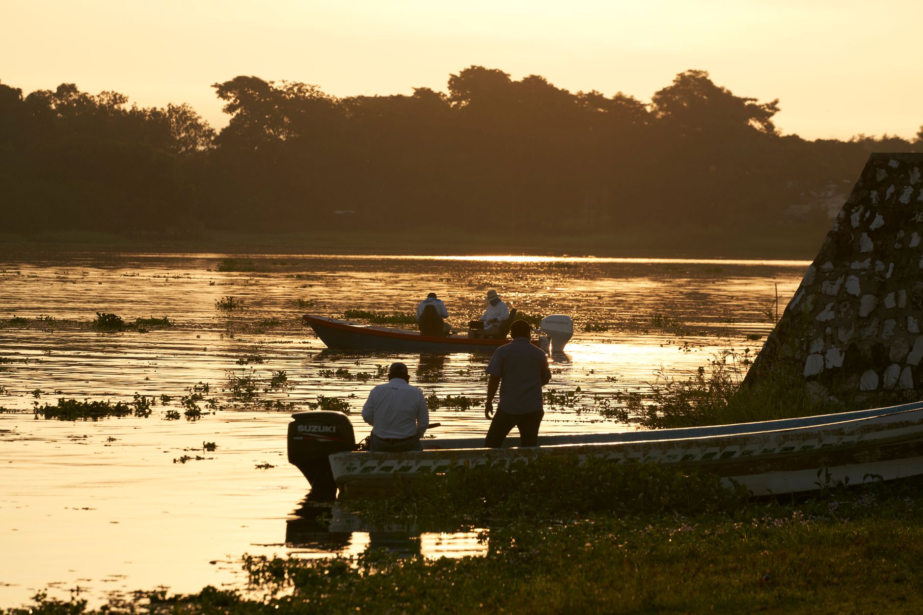 Fishermen in boats at sunset on a calm river, capturing the golden hour's tranquil beauty.