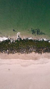 A stunning aerial view of a rocky beach with crashing ocean waves and sandy shore.