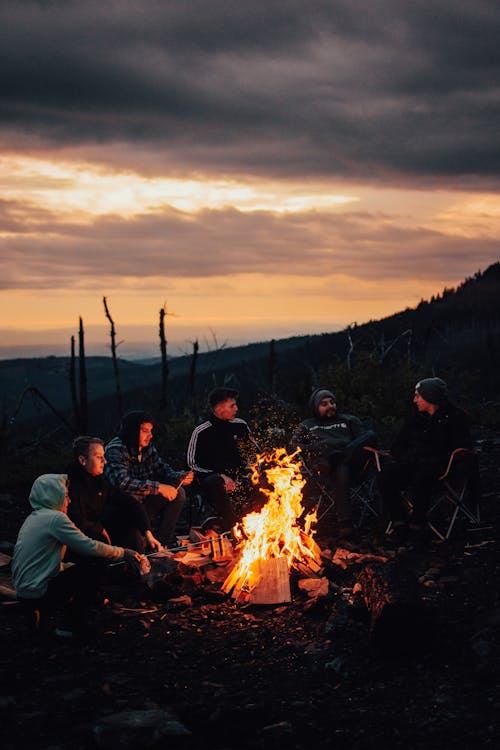 Free People Sitting on Grass Field in front of a Bonfire Stock Photo