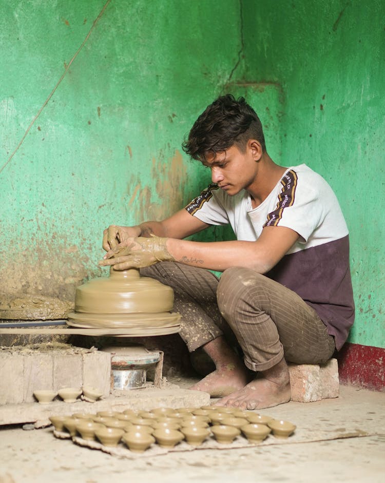 Boy Sitting And Making Cups From Clay On A Pottery Wheel