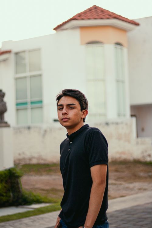 Free Young man in a polo shirt poses confidently outside an urban setting, exuding casual style. Stock Photo