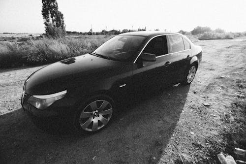 Grayscale Photo of a Car on Dirt Road