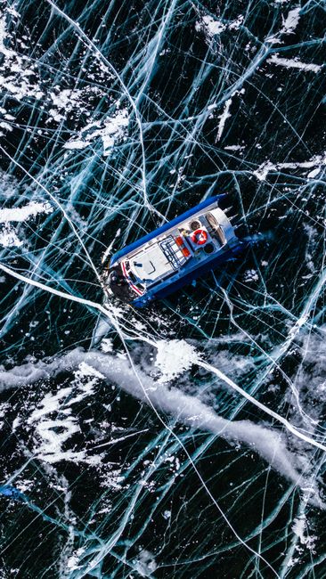 Fotomural Un barco navega por un lago congelado intrincadamente agrietado, capturado desde arriba.