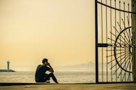 日出时分，一个人沉思着坐在海边，靠近一扇华丽的大门，远处有座灯塔