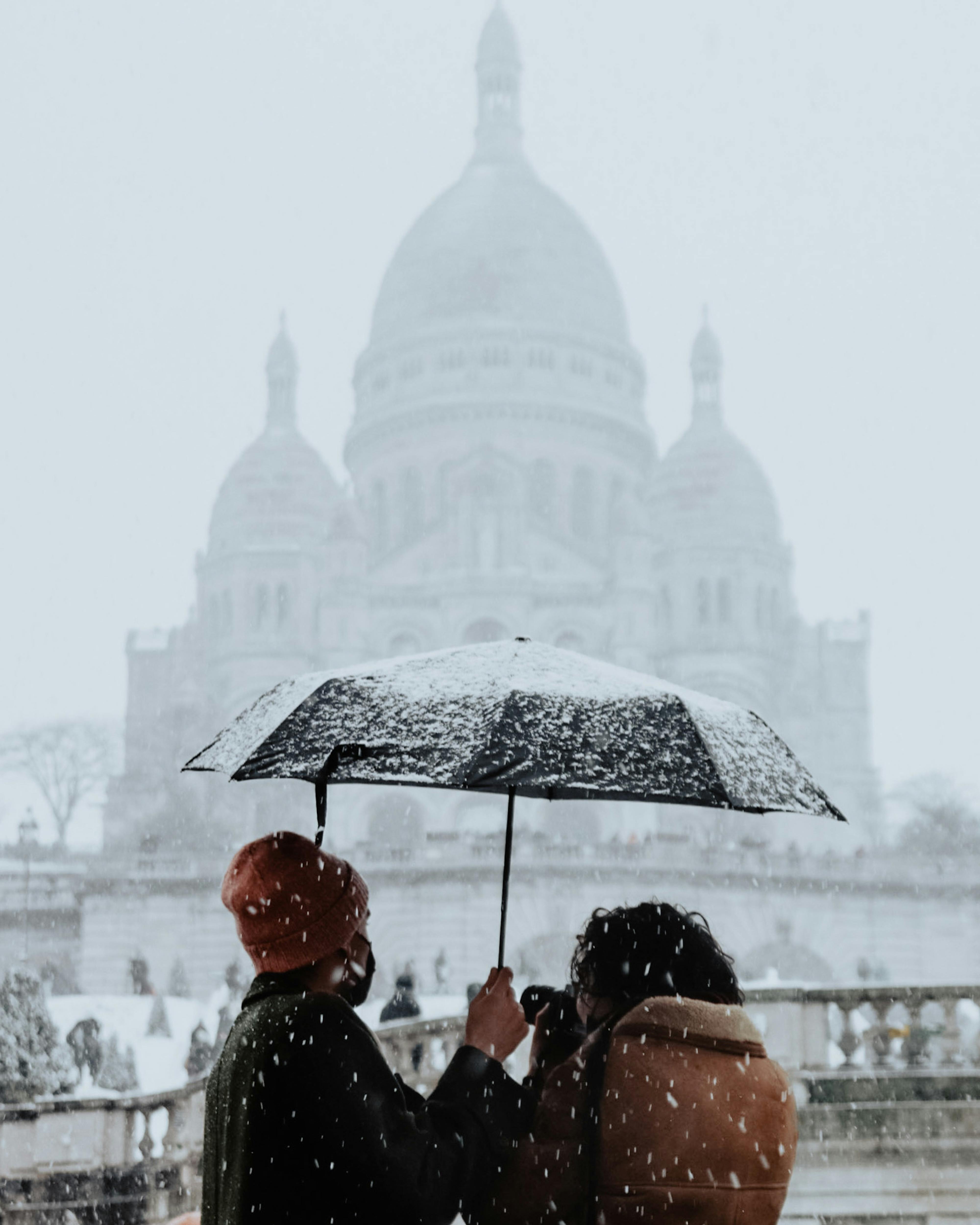 A romantic moment captured at Sacré-Cœur, Paris, under a snowfall.