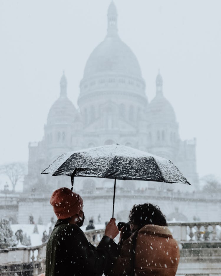 Couple Under Umbrella Looking At The Basilica Of The Sacred Heart On Montmartre In Paris During Snowing