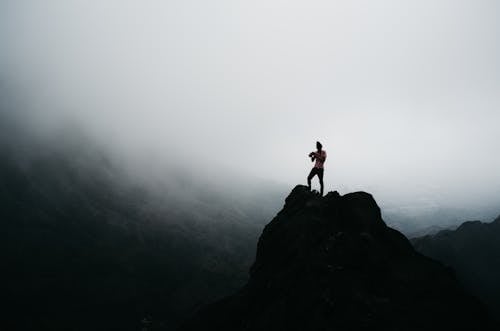 Free Man Standing on Rock Formation on a Foggy Day Stock Photo