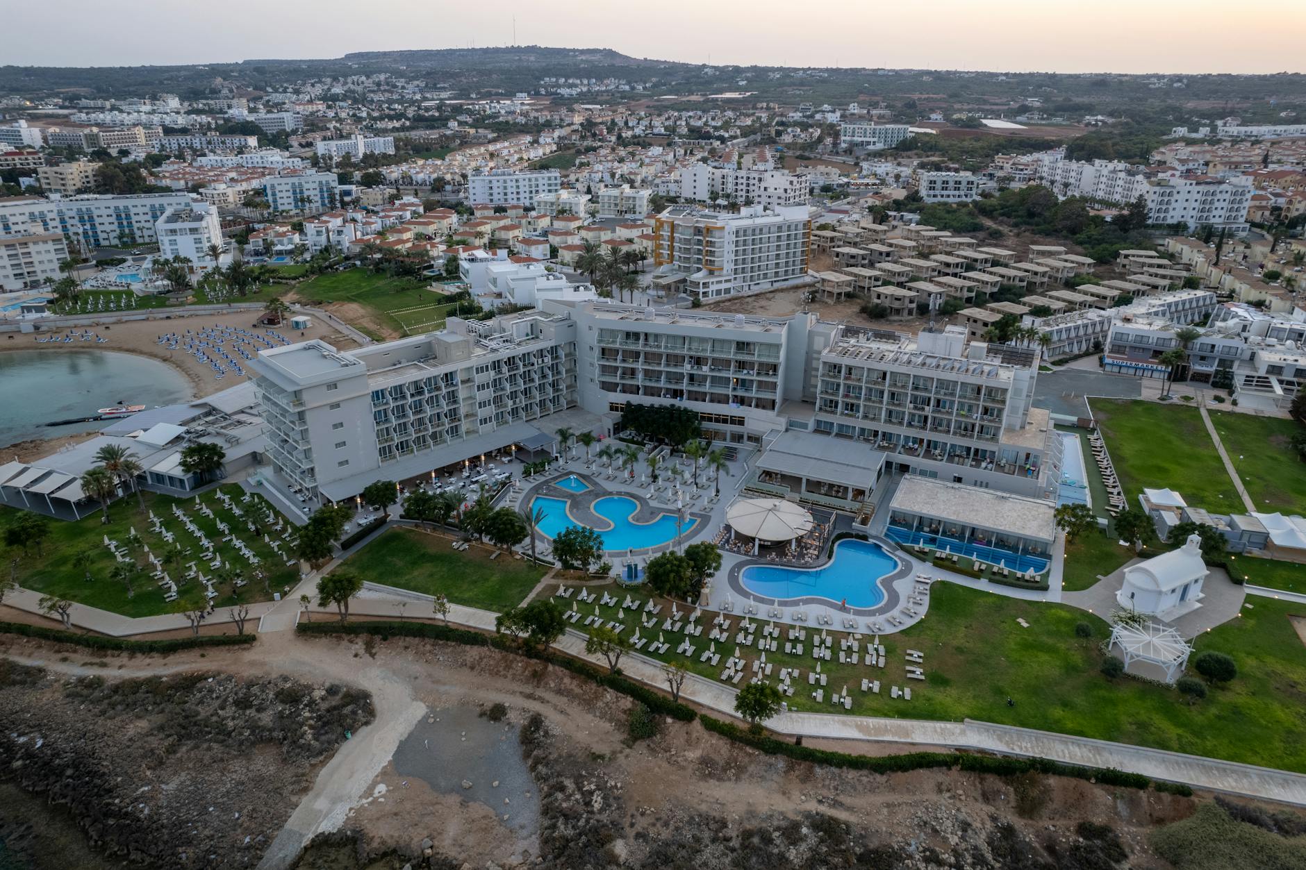 Aerial view of a luxurious resort in Pernera, Famagusta, Cyprus featuring pools and cityscape.