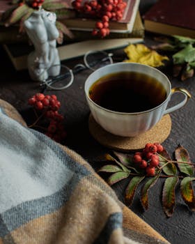 Cozy fall setting with tea, books, rowanberries, and a blanket in warm tones.