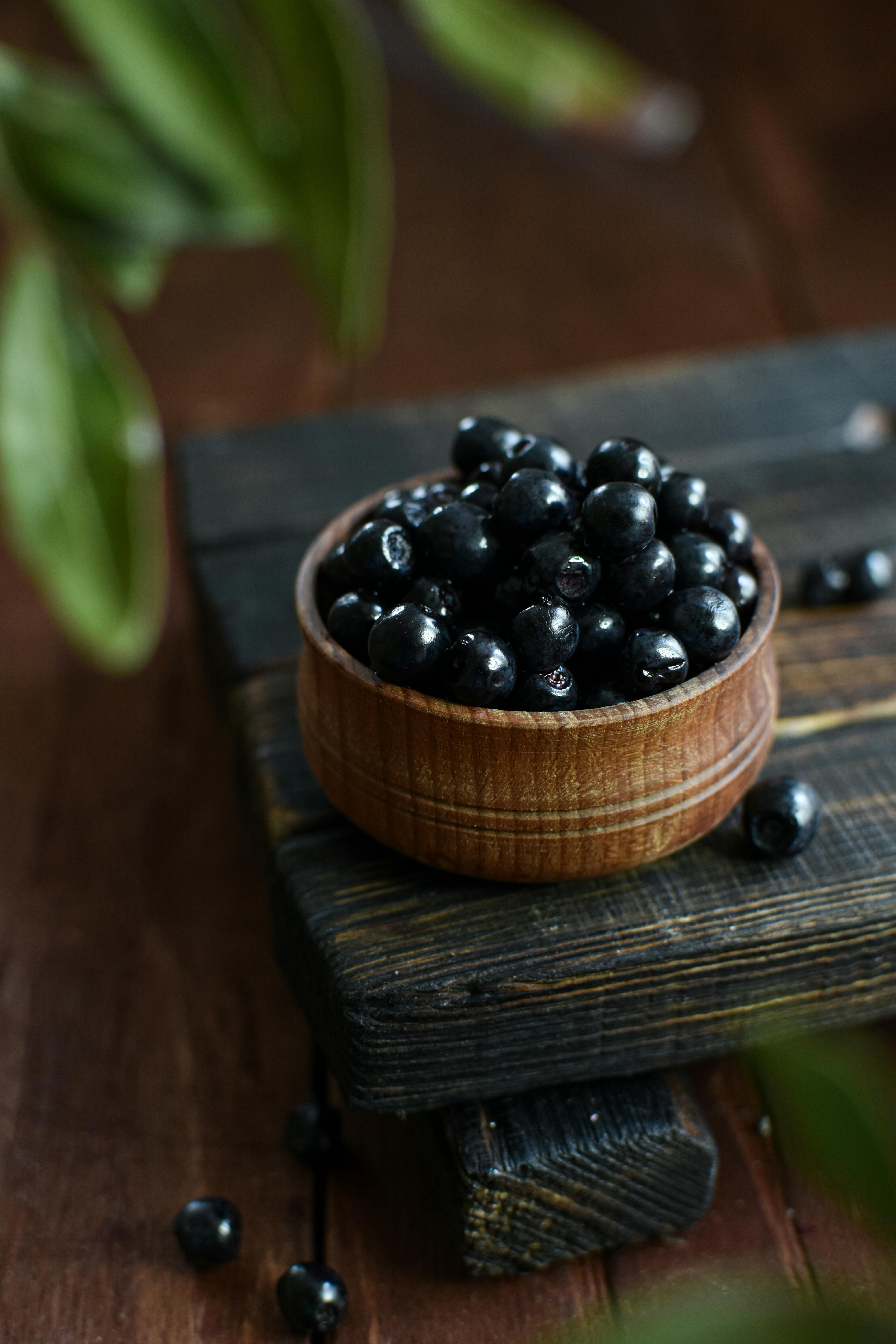 A stylish still life photo of fresh blackcurrants in a wooden bowl on a rustic surface.