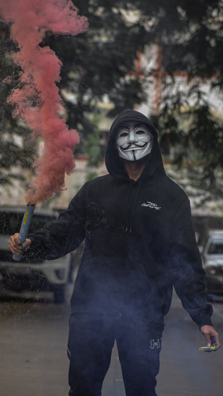 A Person Wearing A White Mask Holding A Smoke Bomb