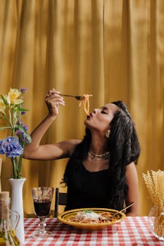Woman elegantly enjoying Italian pasta with wine at a dining table, showcasing foodie lifestyle.