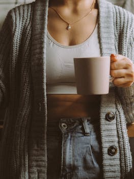 Woman in knit sweater holding a coffee cup, enjoying a cozy indoor setting.